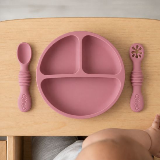 Assiette ventouse bébé coloris rose foncé à compartiments avec cuillère et fourchette assorties, vue de dessus sur tablette en bois