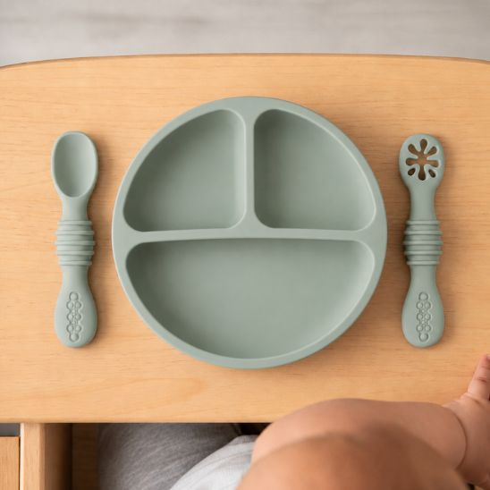 Assiette ventouse bébé coloris sauge à compartiments avec cuillère et fourchette assorties, vue de dessus sur tablette en bois