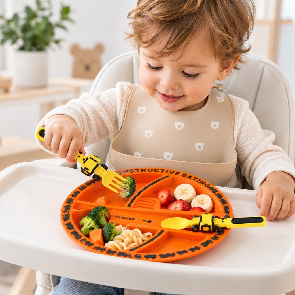 Bébé dans sa chaise haute qui mange seul avec la fourchette pelleteuse de son kit assiette thème chantier